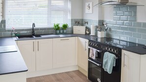 A modern kitchen with a black countertop, white cabinets, a stainless steel sink, and a built-in oven. - 4 bedroom accommodation in Criccieth, near Porthmadog (Criccieth, near Porthmadog)
