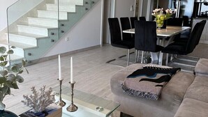 A modern living room with a glass staircase, a dining area with black chairs, and a kitchen with a black refrigerator. - Luxury villa Glory Palm in Makarska, private pool (Makarska)