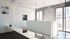 A modern kitchen with white cabinetry, a glass countertop, and a large window providing a view of the city. - Luxury apartment on the top floor with sea view (Puerto Alcudia)