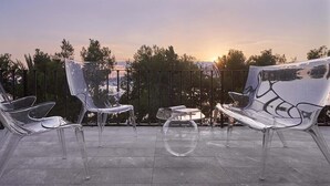 A terrace with clear plastic chairs and a table, overlooking a scenic view with trees and a sunset. - Luxury apartment on the top floor with sea view (Puerto Alcudia)