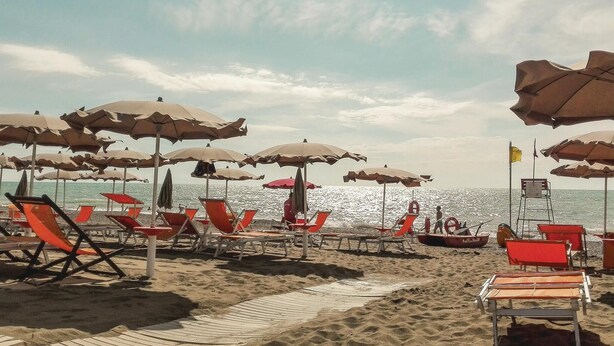 A beach with rows of red and beige beach chairs and umbrellas, a lifebuoy, and a boat named "Natali Mello" in the water. - Cozy home in Cecina Marina with WiFi (Cecina Marina)