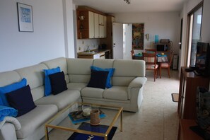 Un salón con un sofá beige, una mesa de centro de vidrio y una televisión.
