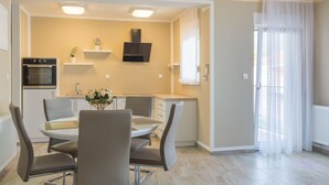 Een moderne keuken met een ingebouwde oven, een eethoek met een ronde tafel en stoelen, en een groot raam met dunne gordijnen.