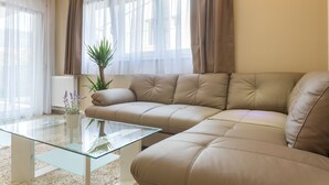 Een woonkamer met een beige bank, een glazen salontafel en een plant in pot.