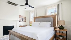 A neatly arranged bedroom with a large bed, a ceiling fan, a bedside table with a lamp, and a window with curtains. - Spacious, Historic Home with Porches (Charleston)