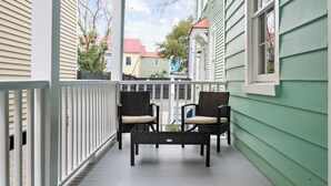 A porch with two wicker chairs and a small table, overlooking a street with colorful houses. - Spacious, Historic Home with Porches (Charleston)