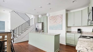 A modern kitchen with a central island, a stainless steel refrigerator, and light green cabinets. - Spacious, Historic Home with Porches (Charleston)