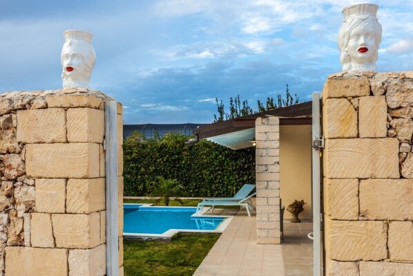 A stone wall with a pool and lounge chairs, leading to a covered area. - 90 sqm flat in villa with individual pool and garden (Siracusa)