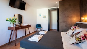 Ein modernes Hotelzimmer mit einem Bett, einem Schreibtisch mit Spiegel, einem Sessel und einem an der Wand befestigten Fernseher.
