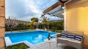 Ein Pool mit Terrasse, einem Korbsessel und einem Tisch mit Flasche und Gläsern.