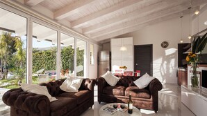 Ein modernes Wohnzimmer mit zwei braunen Ledersofas, einem Glastisch und einer Küchenzeile mit Kühlschrank und Schränken.