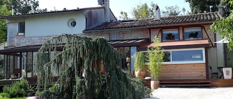 A two-story house with a tiled roof, a large garden with various plants, and a paved driveway.