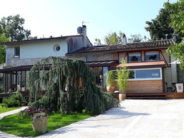 Ein zweistöckiges Haus mit einem Ziegeldach, einem großen Garten mit verschiedenen Pflanzen und einer gepflasterten Auffahrt.