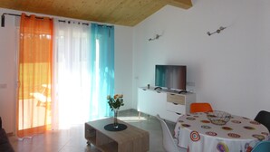 A modern living room with a wooden ceiling, a TV mounted on the wall, a dining table with a colorful tablecloth, and a sofa. - Lodging 4 Gîte RE CLIMATISE IN THE CALM OF THE GREAT VERSENNES  (Saintes)