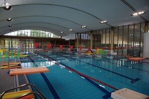An indoor swimming pool with multiple lanes, safety equipment, and a high ceiling with large windows.