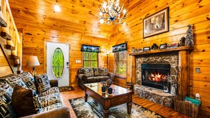 A cozy log cabin interior with a fireplace, a sofa, a coffee table, and a chandelier.