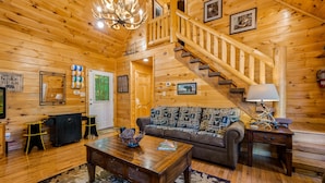 A wooden interior with a staircase, a sofa, a coffee table, and a fireplace.