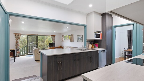 A modern kitchen with dark wood cabinets, a large island, and a dining area with a table and chairs. - Glyndon Family Getaway the perfect family retreat. (VENTNOR)
