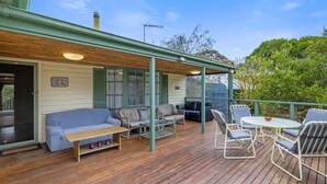 A covered outdoor deck with wooden flooring, a sofa, chairs, and a table. - Glyndon Family Getaway the perfect family retreat. (VENTNOR)