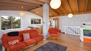 Uma sala de estar moderna com um sofá vermelho, uma cadeira de madeira e uma área de refeições com cozinha ao fundo.
