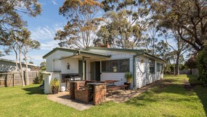 Une petite maison de plain-pied avec un patio, un barbecue et un petit jardin.