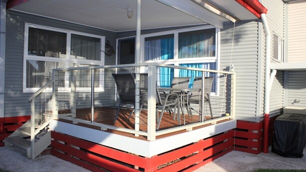 Eine überdachte Terrasse im Freien mit Holzboden, Metallgeländer und einem Tisch mit Stühlen.