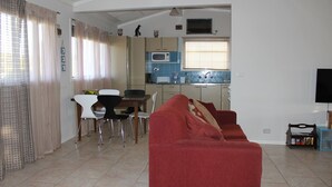 Ein Wohnzimmer mit rotem Sofa, einem Essbereich mit Tisch und Stühlen, einer Küche mit Mikrowelle und einem an der Wand befestigten Fernseher.