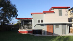 Ein zweistöckiges Haus mit rotem Dach und einer überdachten Terrasse.