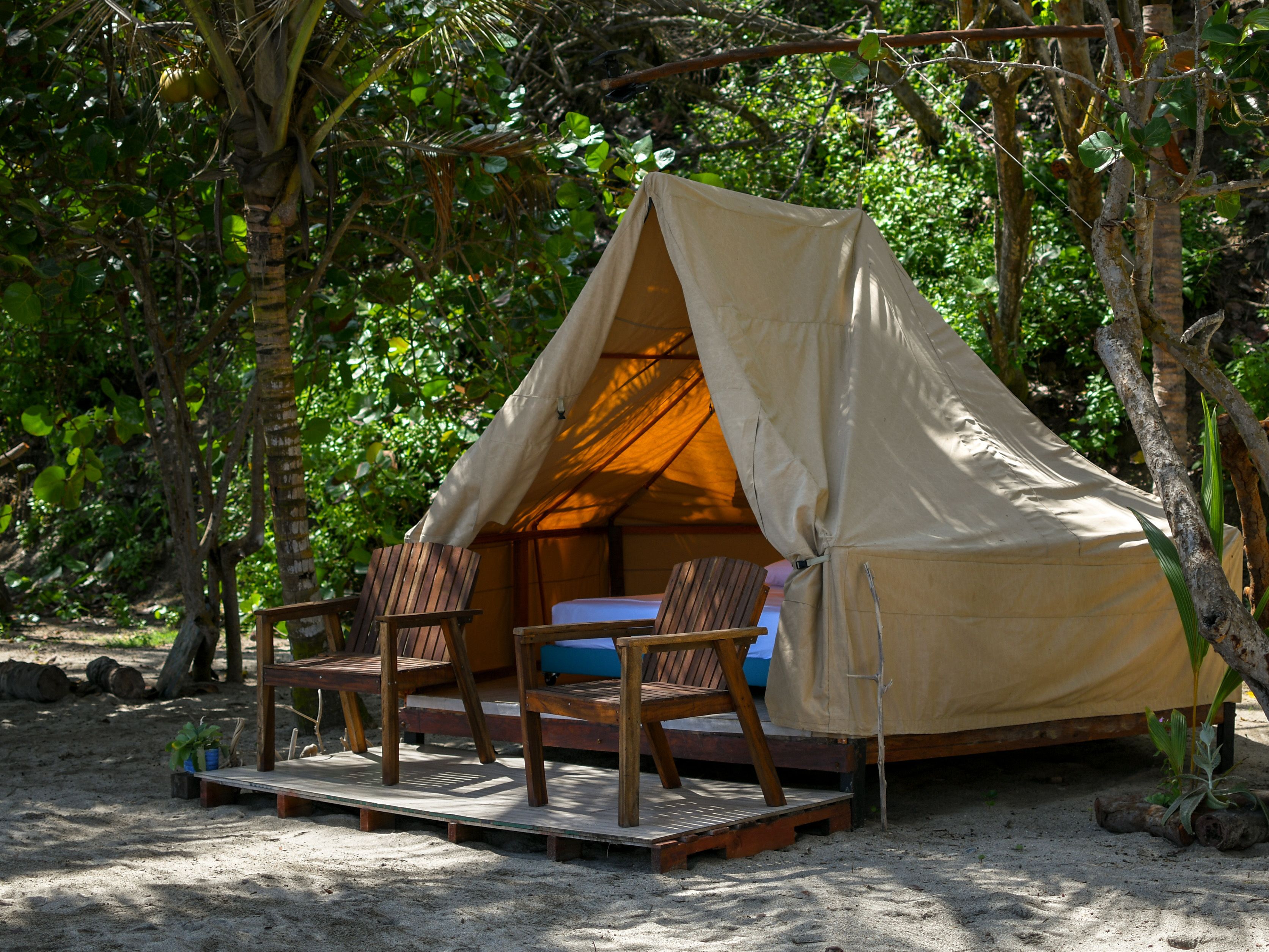 Una carpa con plataforma de madera y dos sillas, rodeada de árboles.
