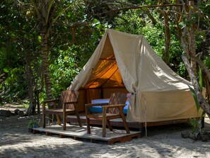 A tent with a wooden deck and two chairs, surrounded by trees.