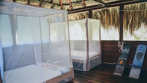 A room with two beds covered by mosquito netting, wooden flooring, and a thatched roof. - Playa Los Angeles (Santa Marta)