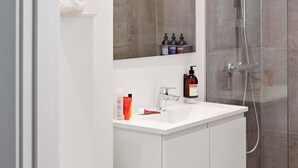 Un bany modern amb plat de dutxa de vidre, un lavabo blanc i un mirall a sobre.