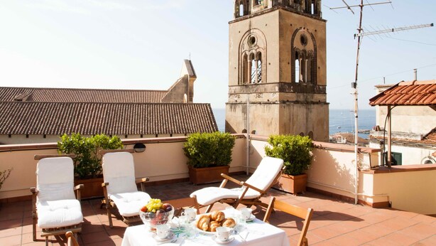 Una terraza con mesa lista para comer, con vistas a una torre histórica y al mar.