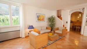 Una sala de estar con mobiliario de mimbre, un ventanal grande y una escalera que conduce a otra habitación.