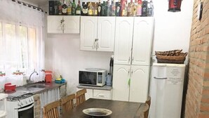 A small kitchen with a wooden table, white cabinets, a microwave, a refrigerator, and a gas stove. - Chácara Vovó Joana (Atibaia)