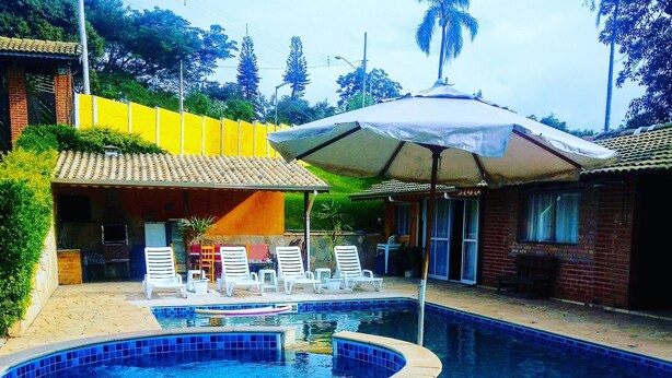 A swimming pool with a tiled edge and a hot tub, surrounded by lounge chairs and an umbrella. - Chácara Vovó Joana (Atibaia)