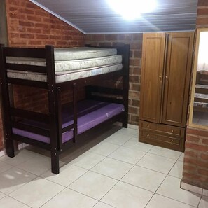 Una habitación pequeña con una cama individual superpuesta, un armario de madera y piso de baldosas.