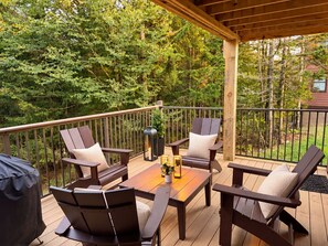 Une terrasse en bois, agrémentée de mobilier d’extérieur, notamment des chaises et une table, et entourée d’une rambarde en métal.