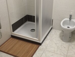 A bathroom with a shower area, a bidet, and a wooden mat.