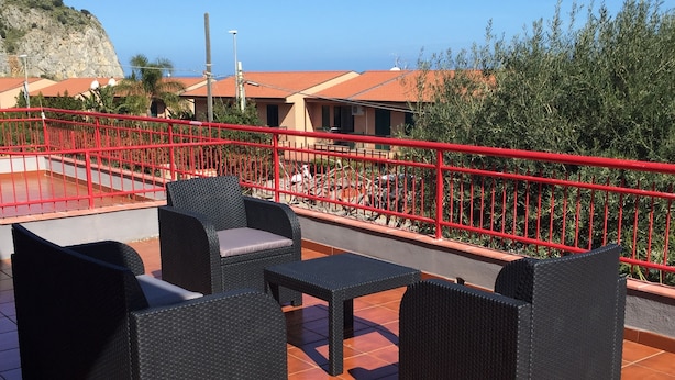 Un patio exterior con mobiliario de mimbre y barandilla roja.