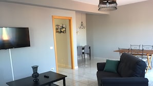 Una sala de estar moderna con un televisor de pantalla plana, una mesa de centro, un sofá y un comedor con mesa y sillas.