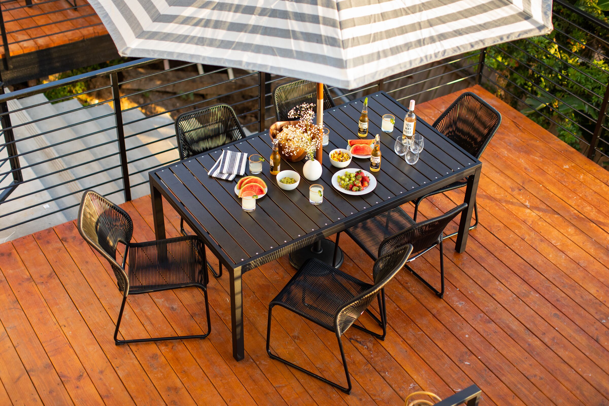 Een terras met een eettafel, omringd door stoelen, en een parasol voor de schaduw.