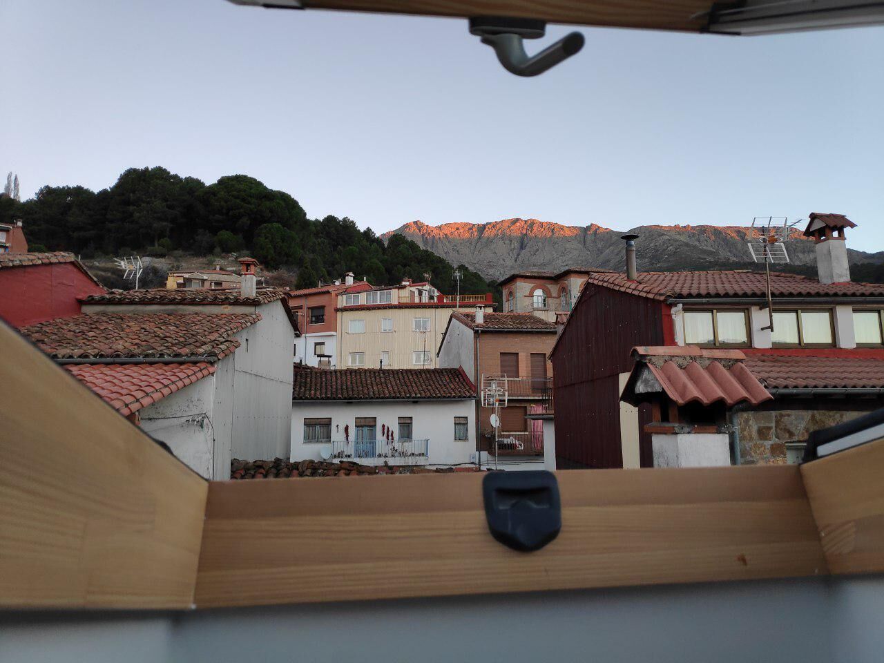 A view from a balcony overlooking a town with terracotta-roofed buildings and a mountain in the background.