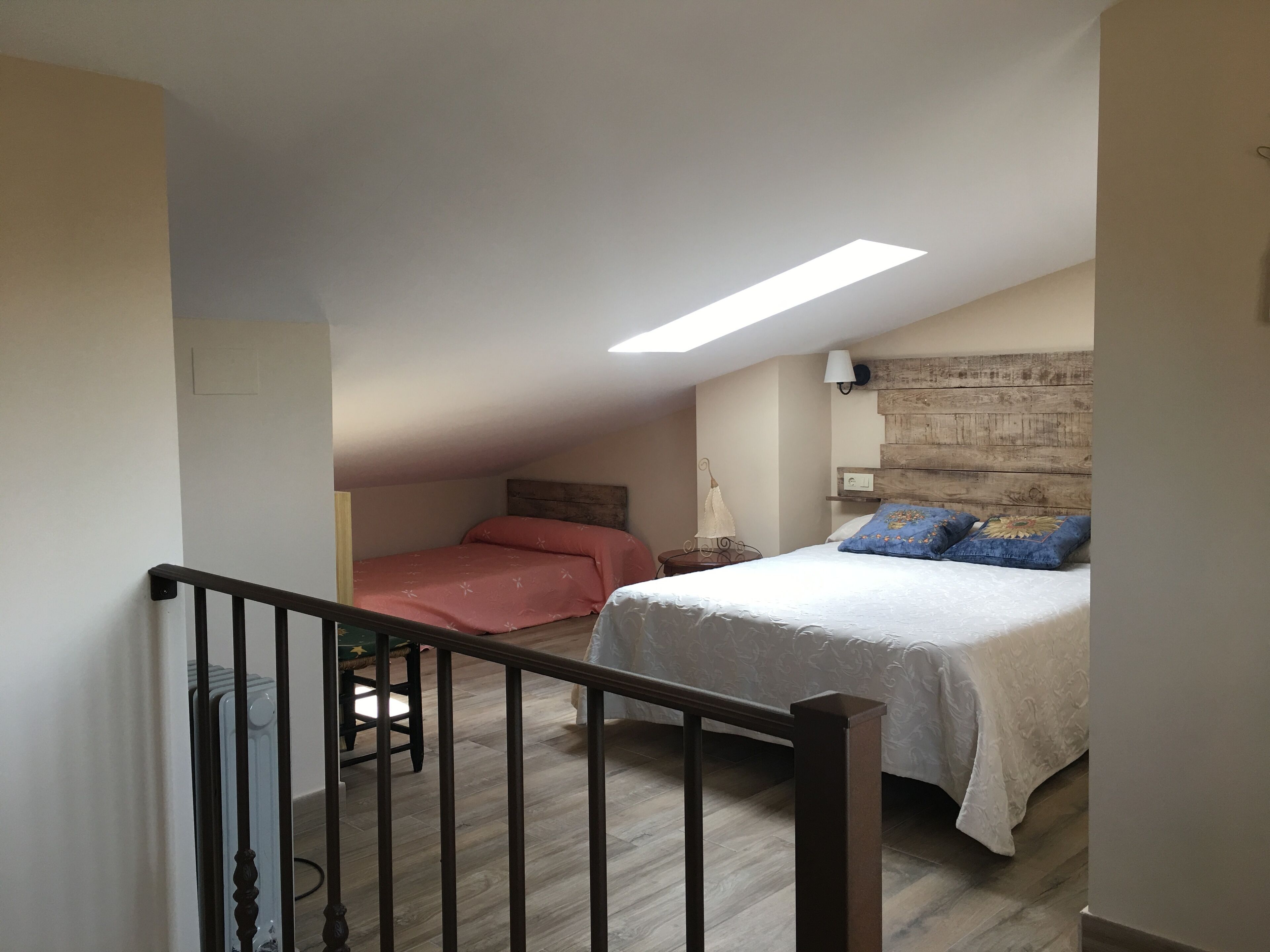 Un dormitorio con techo inclinado, cabecera de madera, cama con ropa de cama blanca, mesita de noche y lámpara.
