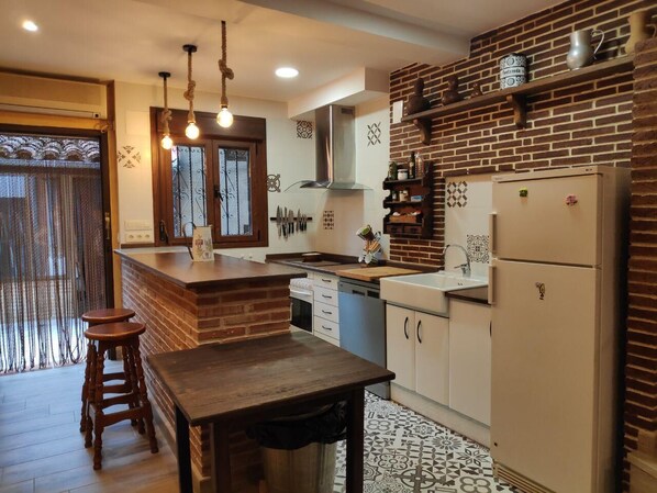Una cocina con isla de madera, luces colgantes, salpicadero de ladrillo y refrigerador.