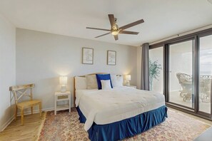 A bedroom with a bed, a ceiling fan, a nightstand, a chair, and a large window.