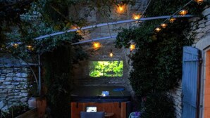 A cozy outdoor seating area with a stone wall, wooden furniture, and string lights. - Welcome to La Maison du Bonheur (Gordes)