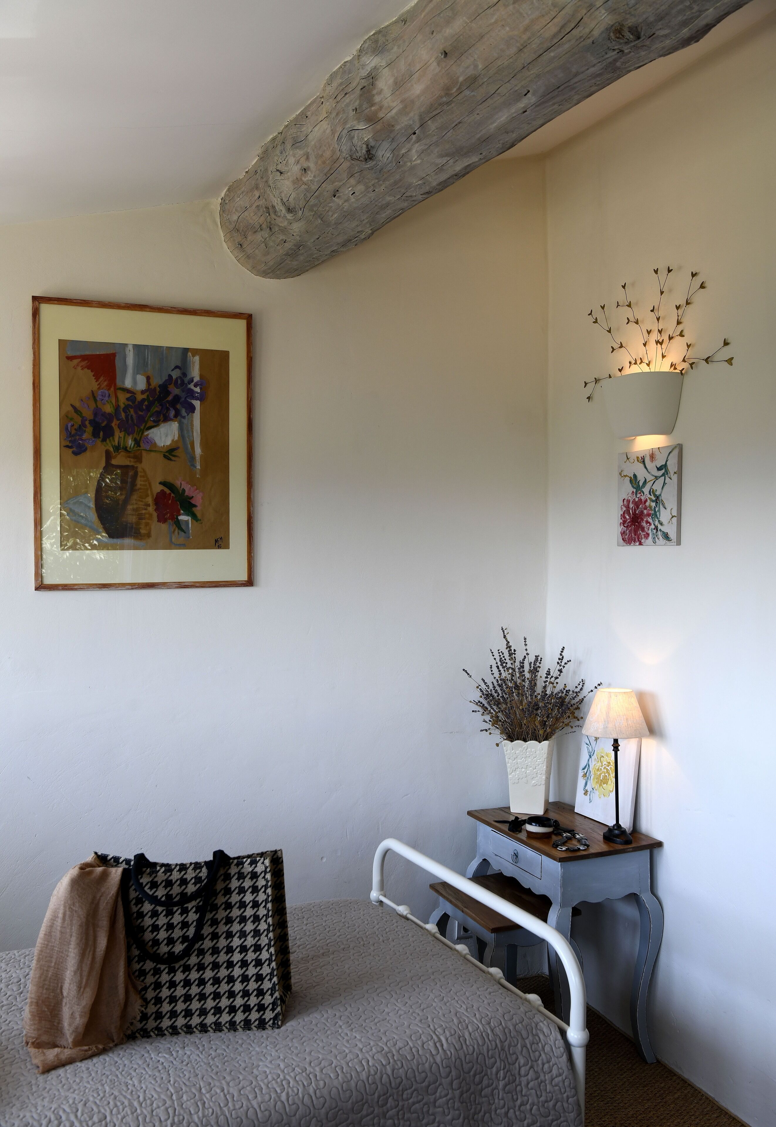 Une chambre à coucher avec un lit, une table de chevet avec une lampe, un tableau encadré et un sac à motifs pied-de-poule.