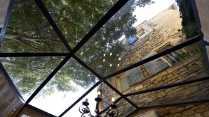 A room with a stone wall, a chandelier, and a view of a building with a blue door. - Welcome to La Maison du Bonheur (Gordes)