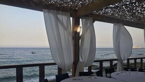 Un área de comedor al aire libre con mesas dispuestas para dos, con vista al mar.